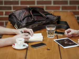 Zwei Personen mit Tablet und Smartphone an Tisch mit Kaffee und Wasser